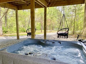 Un jacuzzi bajo una pérgola de madera con sillones colgantes, rodeado de árboles.