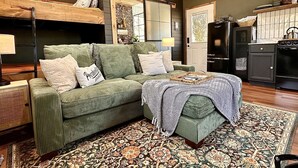 Ein gemütliches Wohnzimmer mit einem grünen Sofa, einem gemusterten Überwurf und einer Holzbalkendecke.