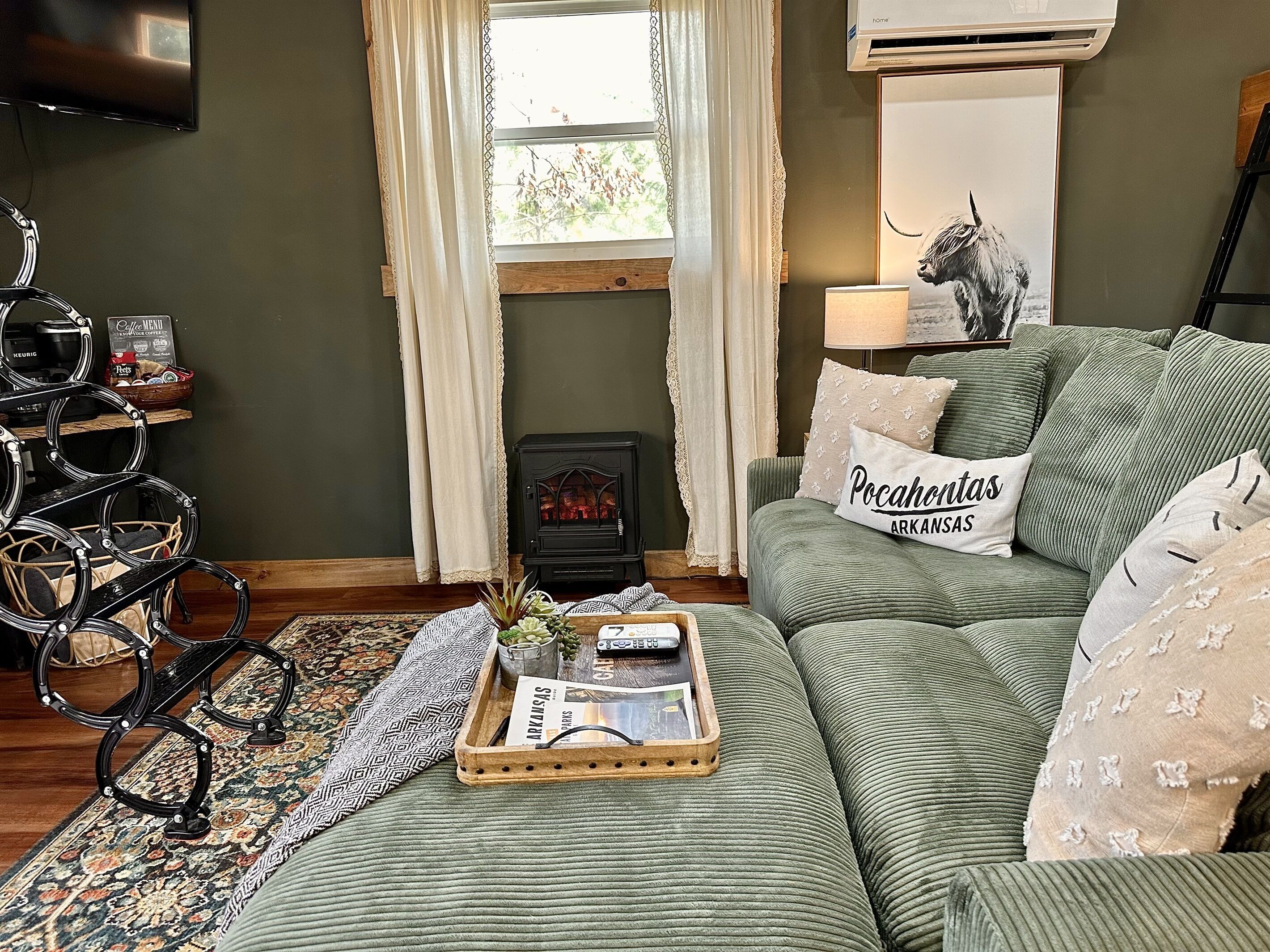 Un salón acogedor con un sofá verde, una mesita de centro con revistas, una lámpara decorativa y un pequeño calentador.