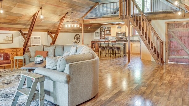 A spacious loft with a high ceiling, exposed wooden beams, a central seating area with a sofa and chairs, a kitchen area, and a staircase leading to an upper level. - Unique, Renovated Barn Vacation Rental in Donnelly (Donnelly)