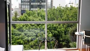 A room with a large window offering a view of dense greenery and urban buildings. - Prime Roma Norte 2BR; Walk to Cibeles, Reforma & Condesa (México D.F.)