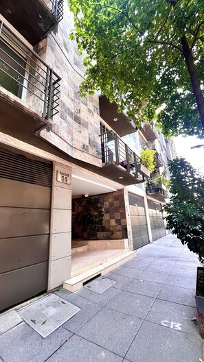 A residential building with a stone facade, a visible garage door, and a tree providing shade. - Prime Roma Norte 2BR; Walk to Cibeles, Reforma & Condesa (México D.F.)
