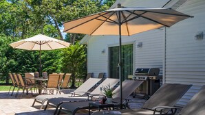Une terrasse extérieure avec des fauteuils de jardin, une table et deux parasols.