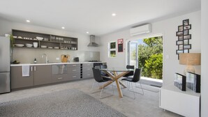 Une cuisine moderne avec des meubles gris, un coin repas doté d’une table en verre et de chaises noires, et une vue sur la verdure à l’extérieur.