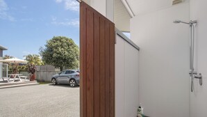 Une porte en bois donne accès à un espace douche avec un mur blanc et une pomme de douche visible.