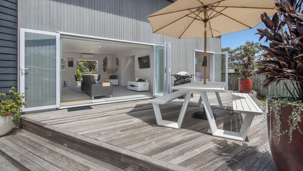 Une terrasse ouverte avec une table et des chaises, un grand parasol et une plante en pot.