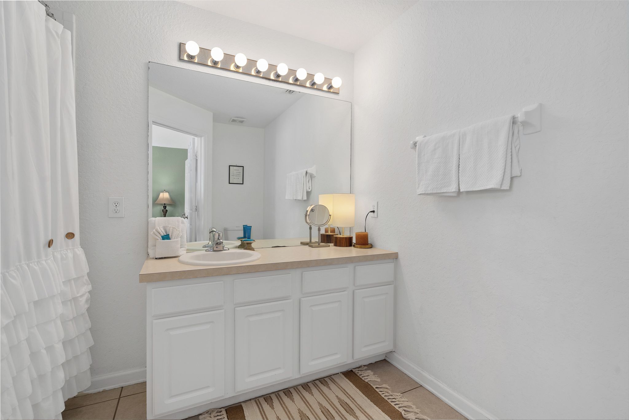 Une salle de bain avec un meuble-lavabo, un miroir avec éclairage intégré, un porte-serviettes et un tapis.