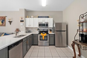 A modern kitchen with white cabinets, stainless steel appliances, and a tiled floor.