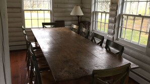 Une grande table à manger en bois, entourée de chaises, placée dans une pièce aux murs en bois et aux grandes fenêtres.
