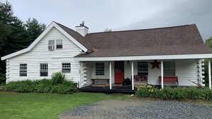 Une cabane en rondins blanchie, dotée d’un porche, d’une porte rouge et d’une décoration en forme d’étoile.