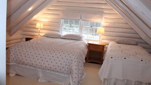 Une chambre confortable située sous les toits, avec un plafond en pente, deux tables de chevet avec des lampes, un grand lit avec une literie à motifs floraux et une fenêtre donnant sur l’extérieur.
