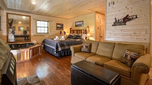 Una habitación tipo cabaña de troncos con una cama, un sofá, una mesa de centro, un espejo y un cartel de bienvenida.