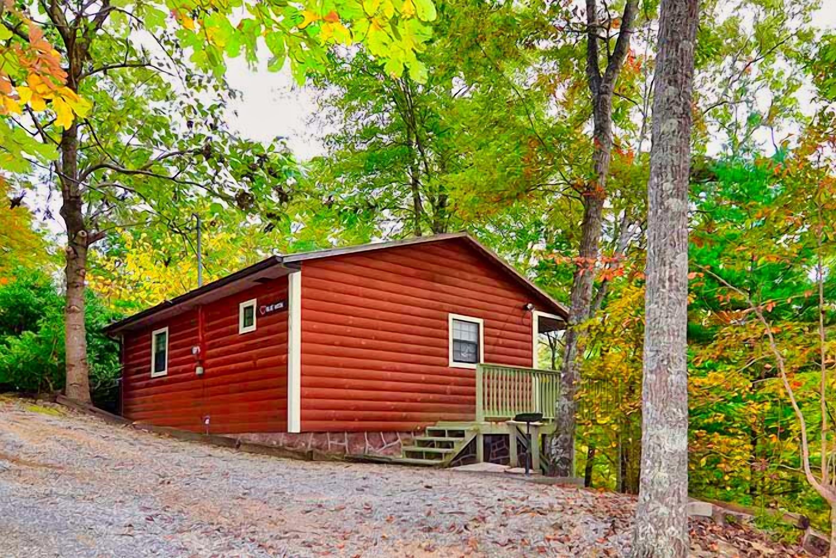 A red log cabin with a wooden deck and a stone pathway leading to it.