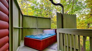 Un jacuzzi en una terraza de madera, con un cerco de madera y árboles al fondo.