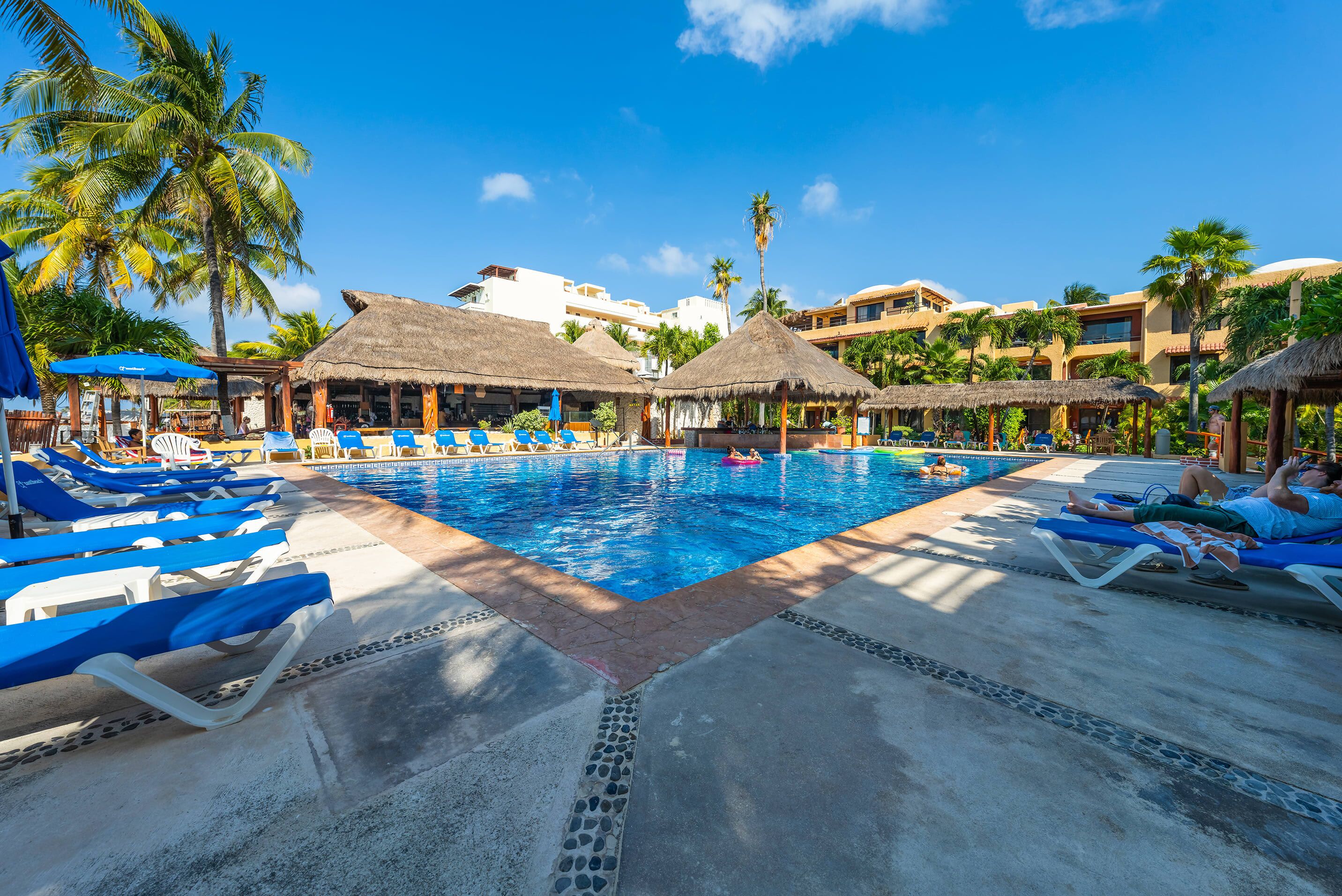 A pool area with lounge chairs, thatched-roof structures, and palm trees.