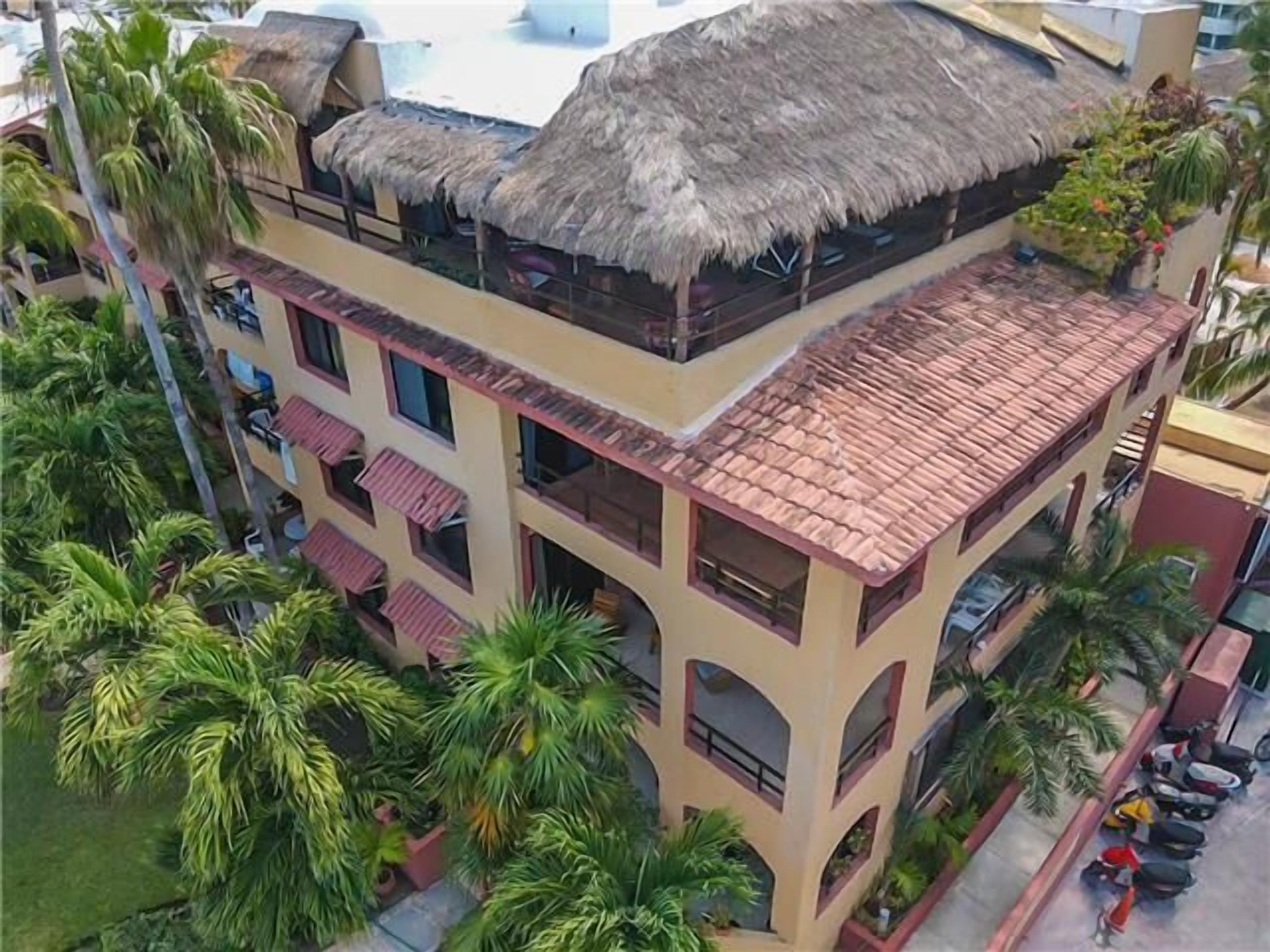 A multi-story building with a thatched roof, balconies, and a pool.