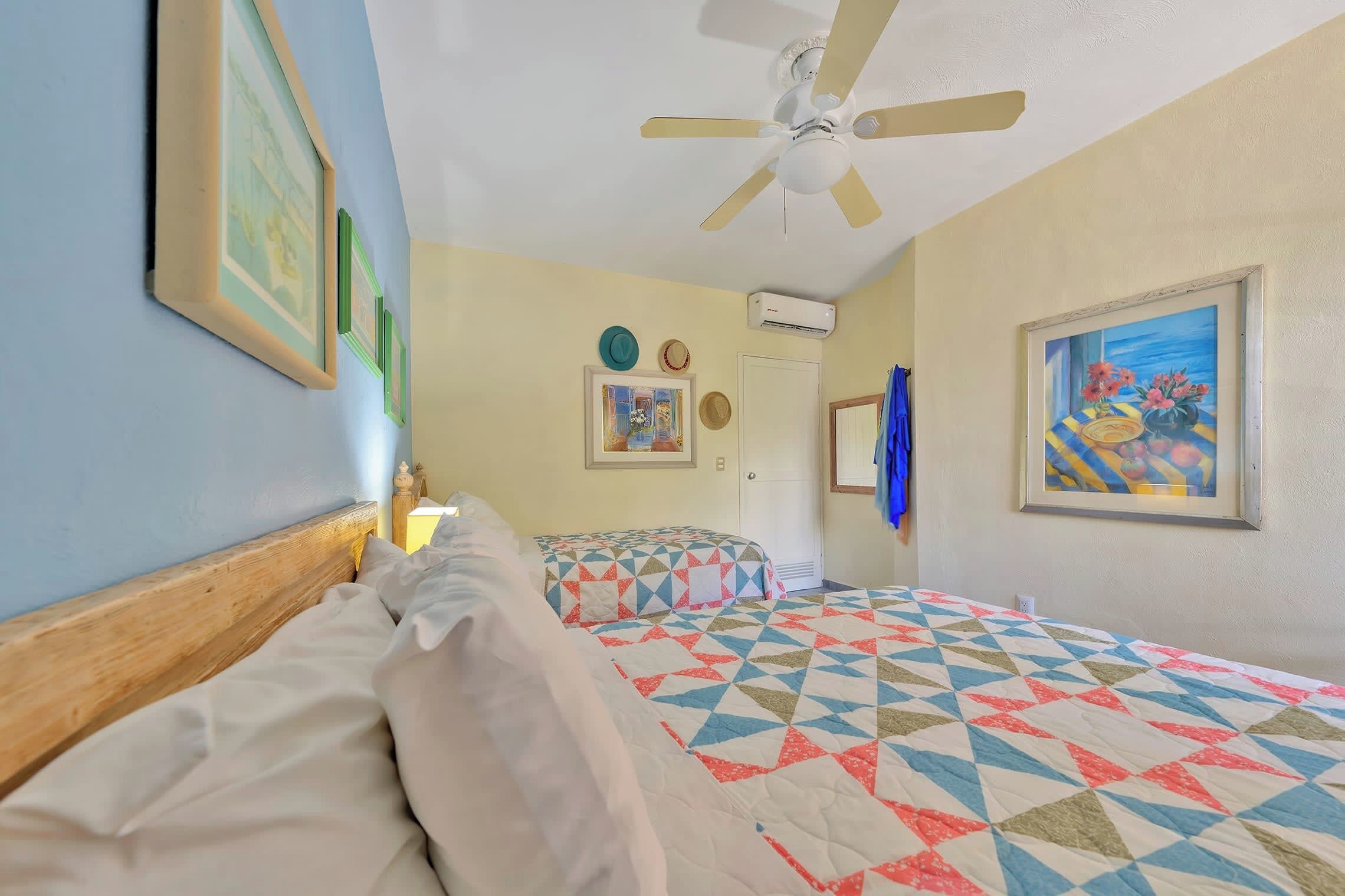 A hotel room with two beds, a ceiling fan, and artwork on the walls.