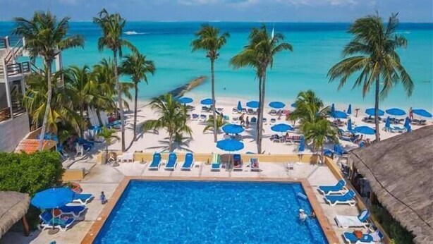 A poolside view of a resort with a clear view of the ocean, palm trees, and beach umbrellas. - Nautibeach Condo 22  – 2 Bedroom, Family-Friendly Vacation on the Beachfront Third-Floor (Isla Mujeres)