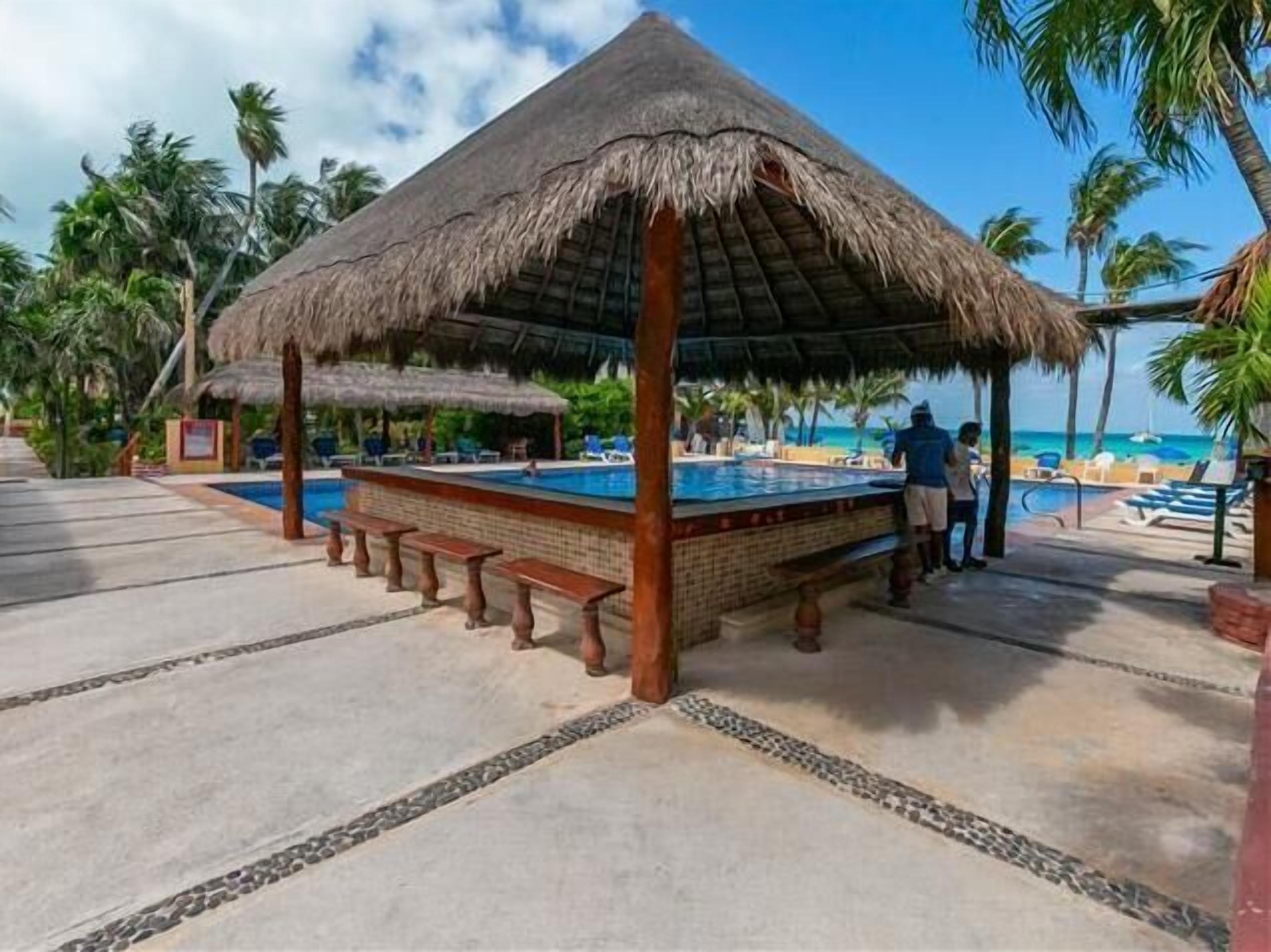A pool area with a thatched roof structure, lounge chairs, and a view of the beach.