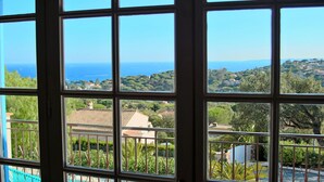 A view through a window with a balcony, overlooking a coastal landscape with houses and greenery. - SUPERB VILLA (220m2), SEA AND VIEW BETWEEN ST MAXIME AND ISSAMBRES (Sainte-Maxime)