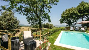 Area piscina con mobili in vimini e vista sulla campagna.