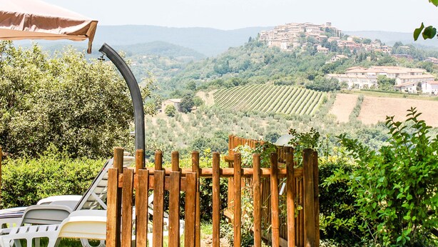 Vista su un vigneto con una recinzione in legno, una sedia bianca e un ombrello beige.