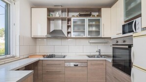 A modern kitchen with wooden cabinets, a Bosch dishwasher, a microwave, and a stove. - Beachfront apartment with Infinity Pool & BBQ (Slatine)