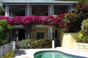 A hotel with a pool, covered outdoor seating, and vibrant bougainvillea flowers.