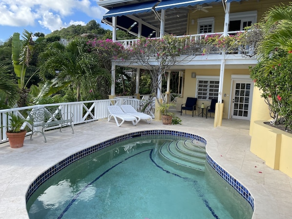A pool area with a curved edge, white lounge chairs, and a covered patio with a ceiling fan.