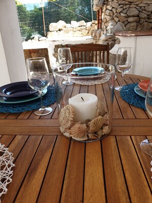 A wooden table with a candle centerpiece surrounded by seashells, clear glass candle holders, and blue and red plates. - VILLA PLUMBAGO (Porto Rotondo / Cugnana) (Olbia)