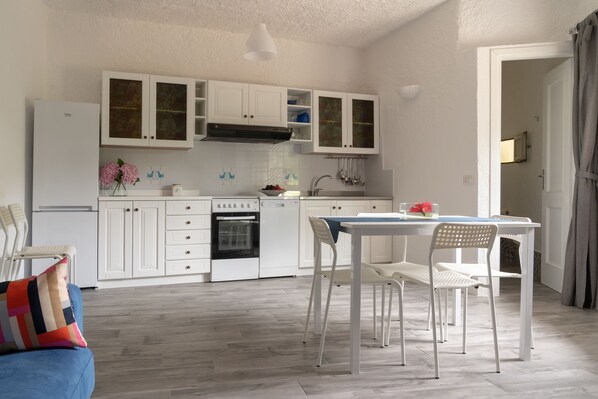 A modern kitchen with white cabinetry, a dining area with a table and chairs, and a visible oven and sink. - VILLA PLUMBAGO (Porto Rotondo / Cugnana) (Olbia)