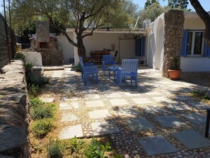A stone patio with outdoor furniture, a stone fireplace, and a tree providing shade. - VILLA PLUMBAGO (Porto Rotondo / Cugnana) (Olbia)
