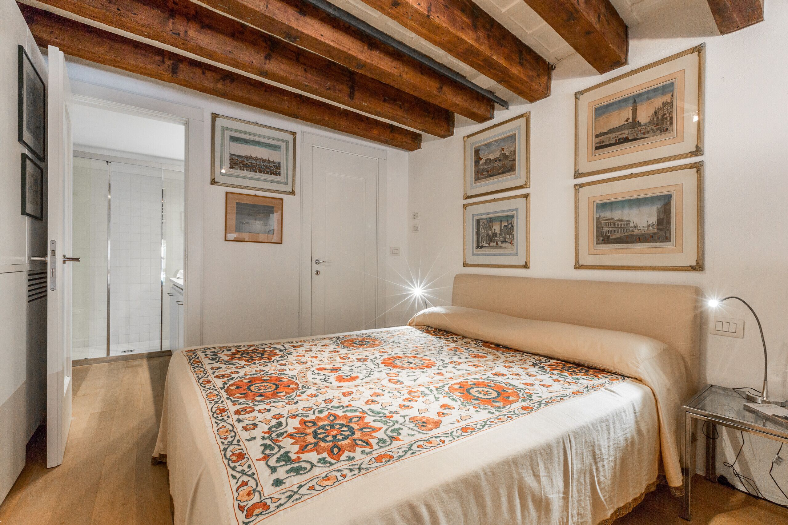 Un dormitorio con cama, vigas de madera, una puerta y cuadros en la pared.