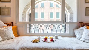 A neatly made bed with a breakfast tray, a window with a view of a building, and framed pictures on the wall. - Ca' Tintoretto (Venice)