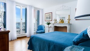 Quarto com cama grande, uma cadeira, cômoda, lareira e varanda com guarda-corpo.