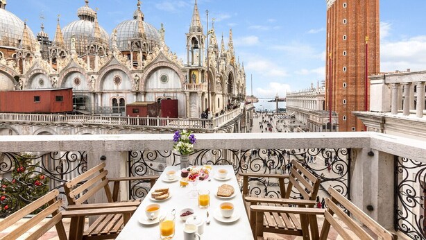 Terraço com mesa posta para café da manhã, com vista para um edifício histórico de arquitetura elaborada.