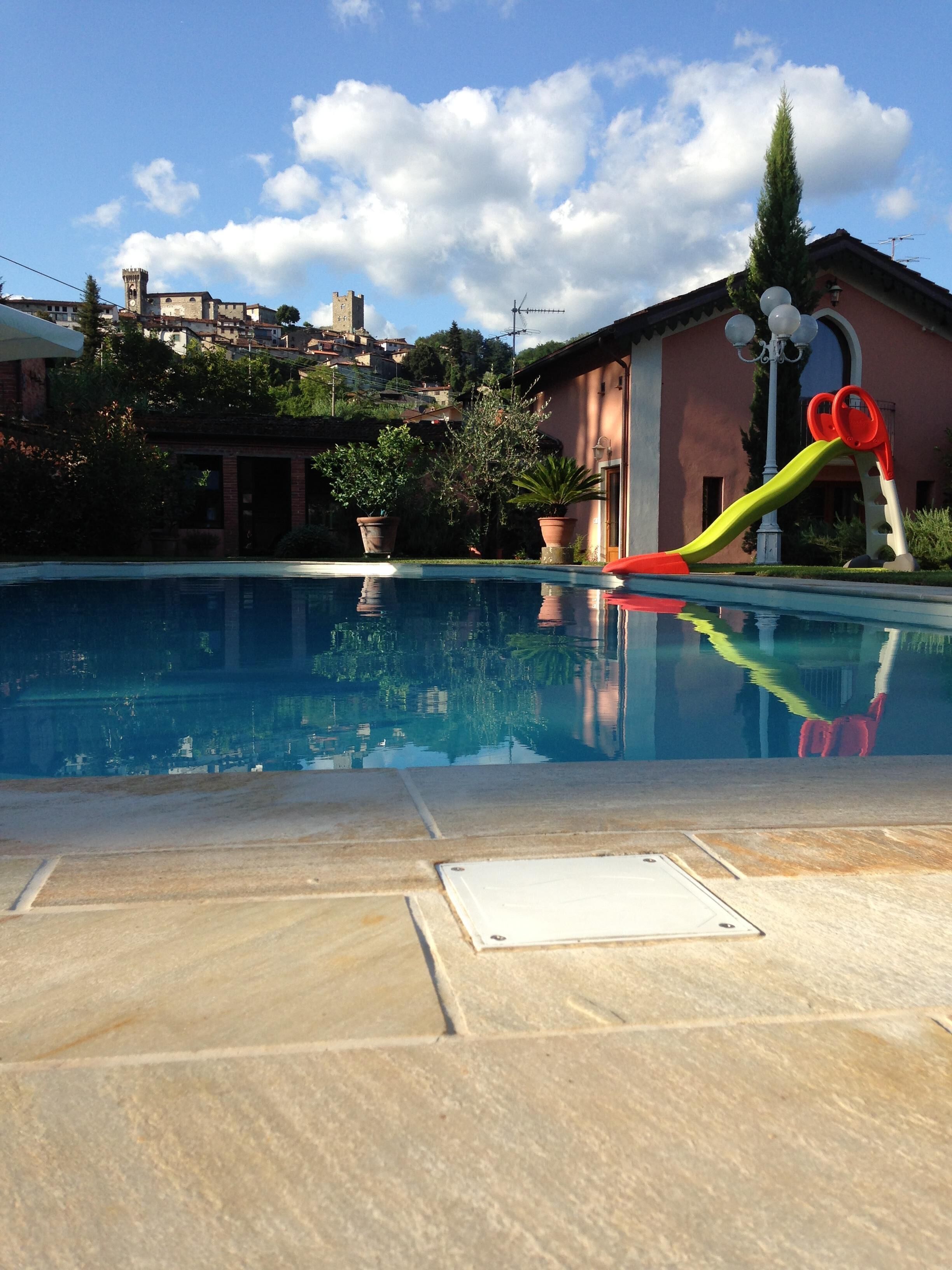 Una piscina con tobogán, rodeada por un patio con baldosas de piedra.