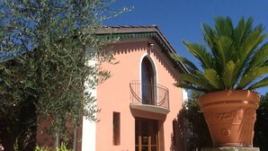Un edificio con fachada rosa, un balcón con barandilla de metal y una planta grande en maceta al frente.