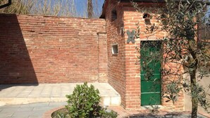 Un edificio de ladrillo con una puerta verde, un pequeño jardín con un arbusto y un árbol.