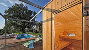 Un sauna en bois, équipé d’un banc et d’une serviette, situé à côté d’un espace piscine avec des chaises longues.