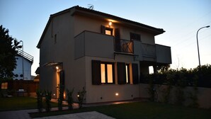 A modern two-story house with a balcony, a small garden, and a paved driveway. - Seaside house with private garden (Follonica)