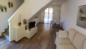 A modern living space with a staircase, a sofa, a dining area, and a kitchen. - Seaside house with private garden (Follonica)
