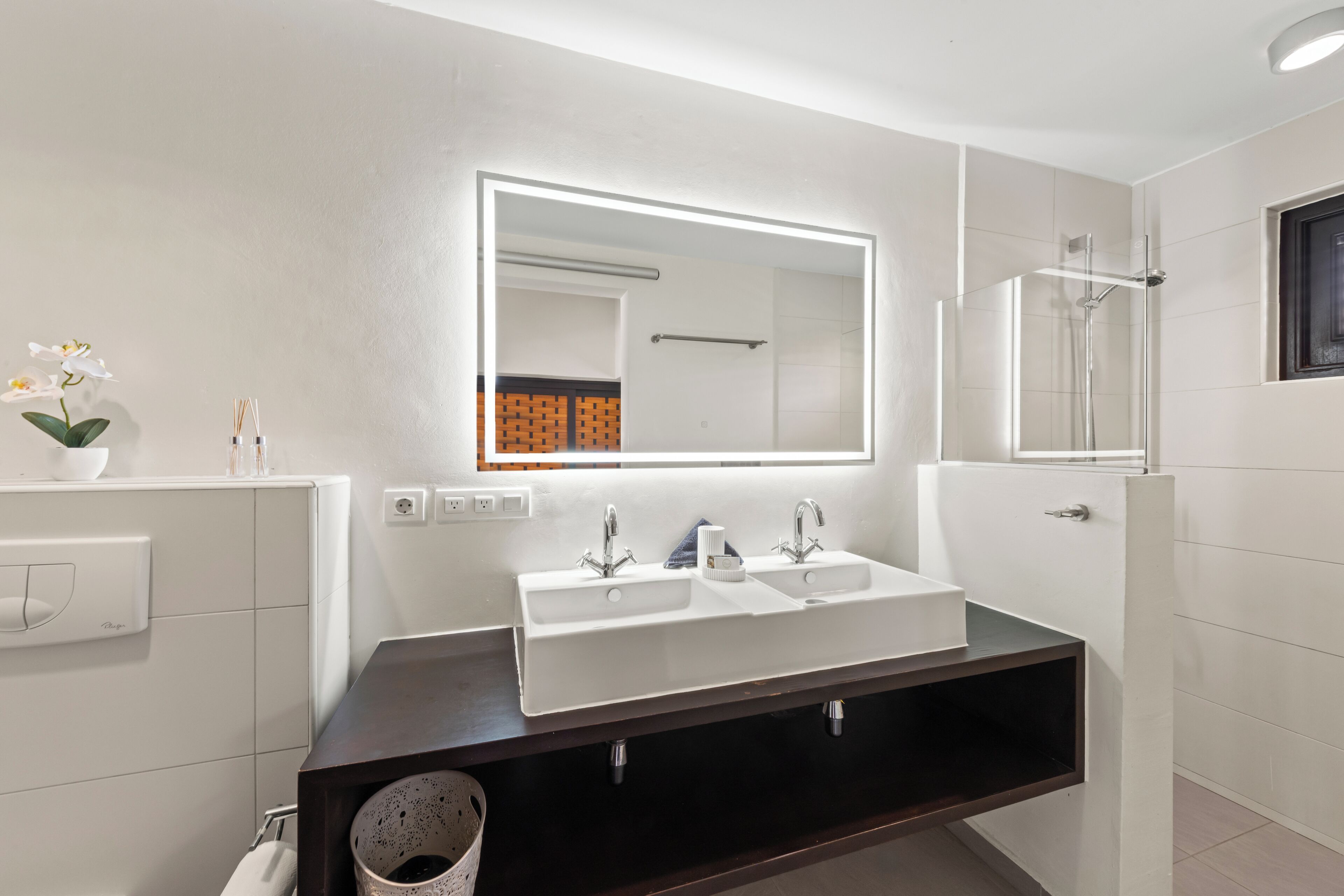 A modern bathroom with a double sink vanity, a large mirror, and a shower area.