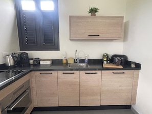 A kitchen with a black countertop, wooden cabinets, a stainless steel sink, a coffee maker, and a kettle.