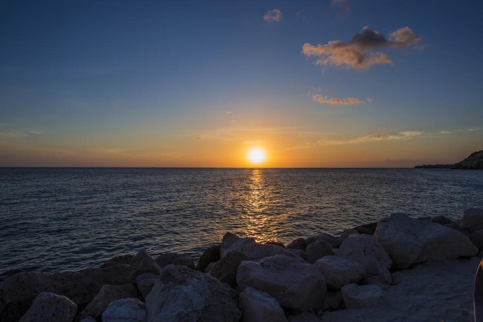 Ein Sonnenuntergang über dem Meer mit einer felsigen Küste im Vordergrund.