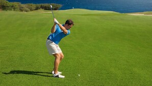 Una persona juega al golf sobre un césped con vista al océano.