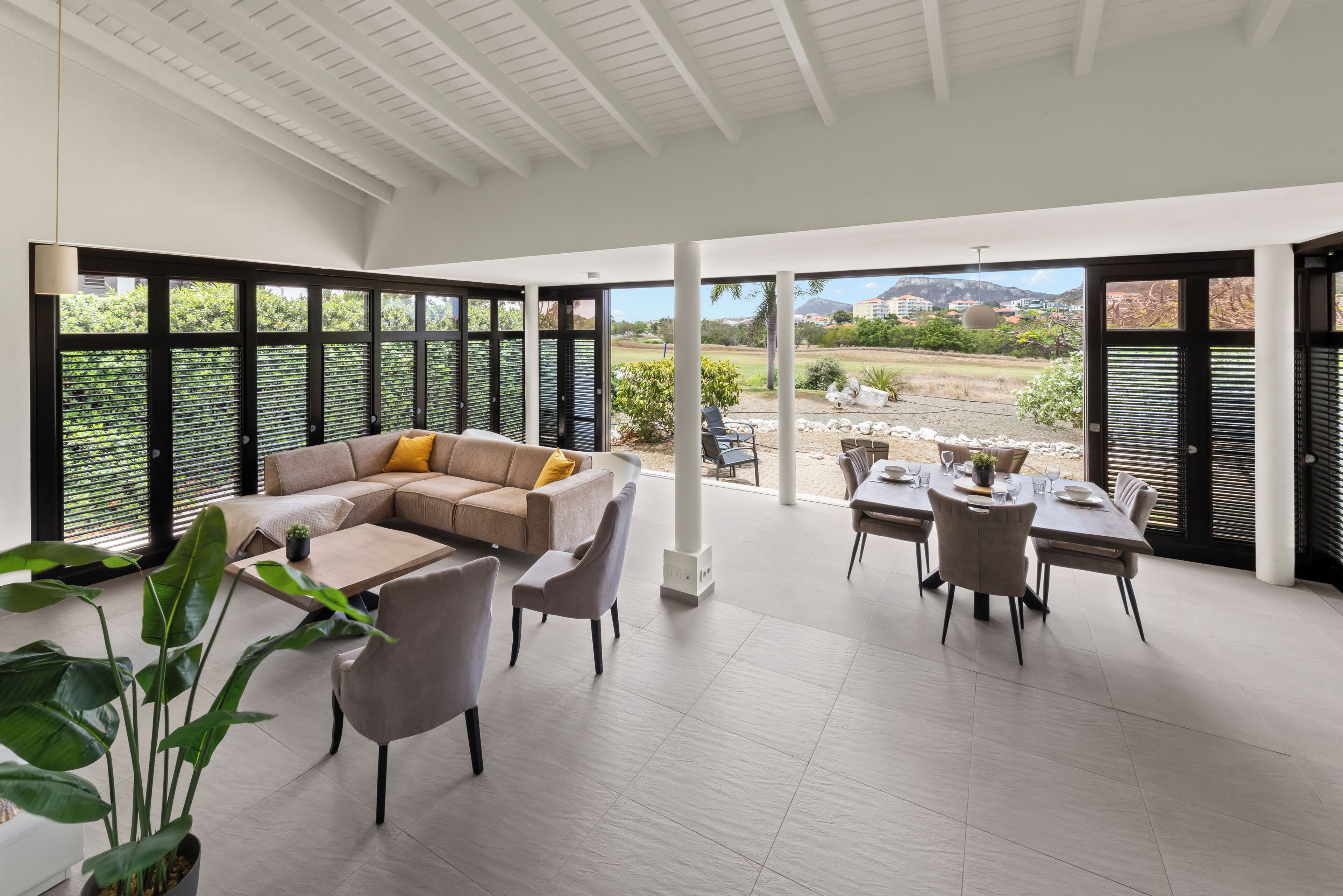 A spacious room with a large window, a sofa, a dining table, and chairs.