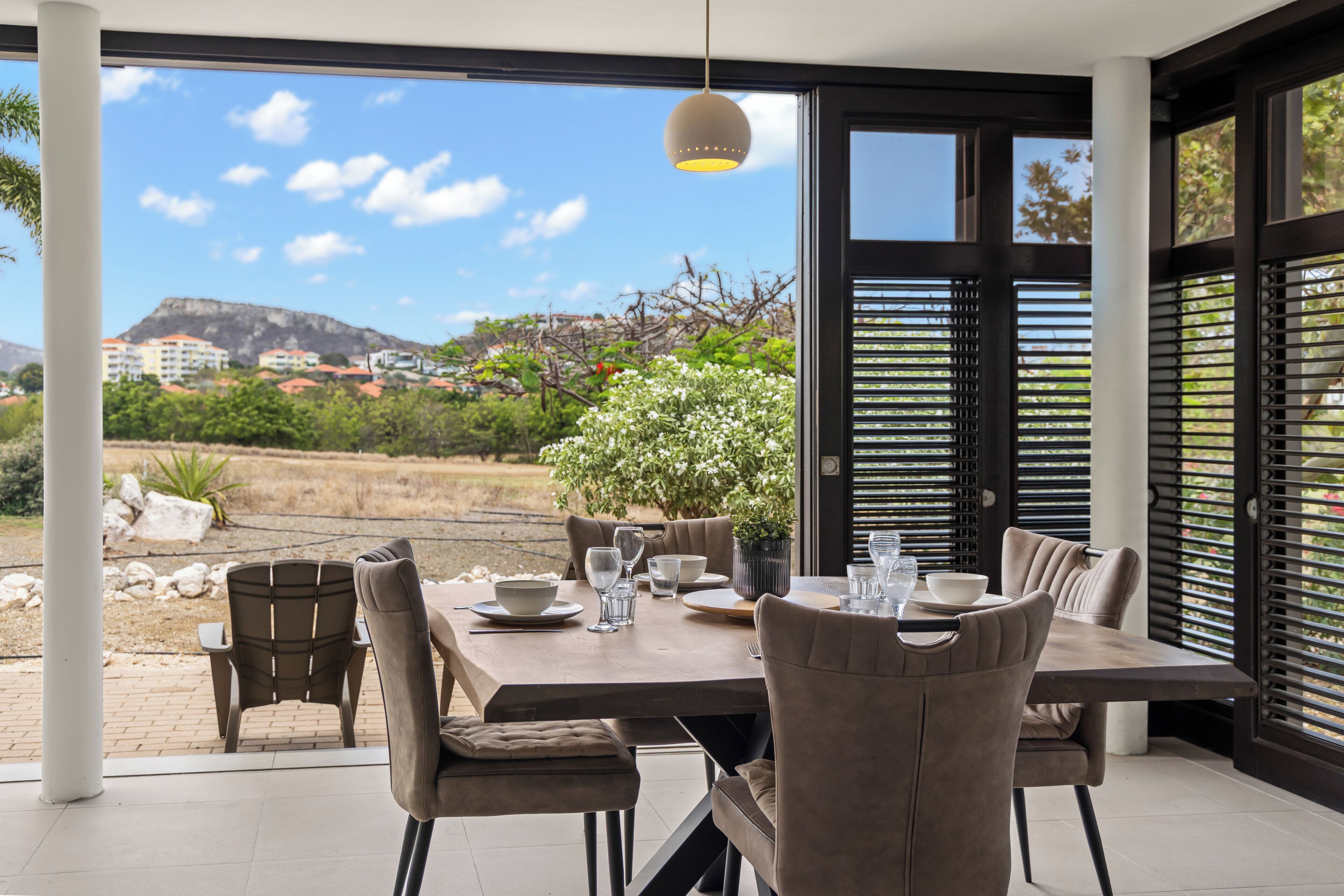 Un espace extérieur aménagé pour prendre les repas, avec une table dressée pour quatre personnes, entourée de chaises, et offrant une vue sur un paysage montagneux et des bâtiments situés au loin.