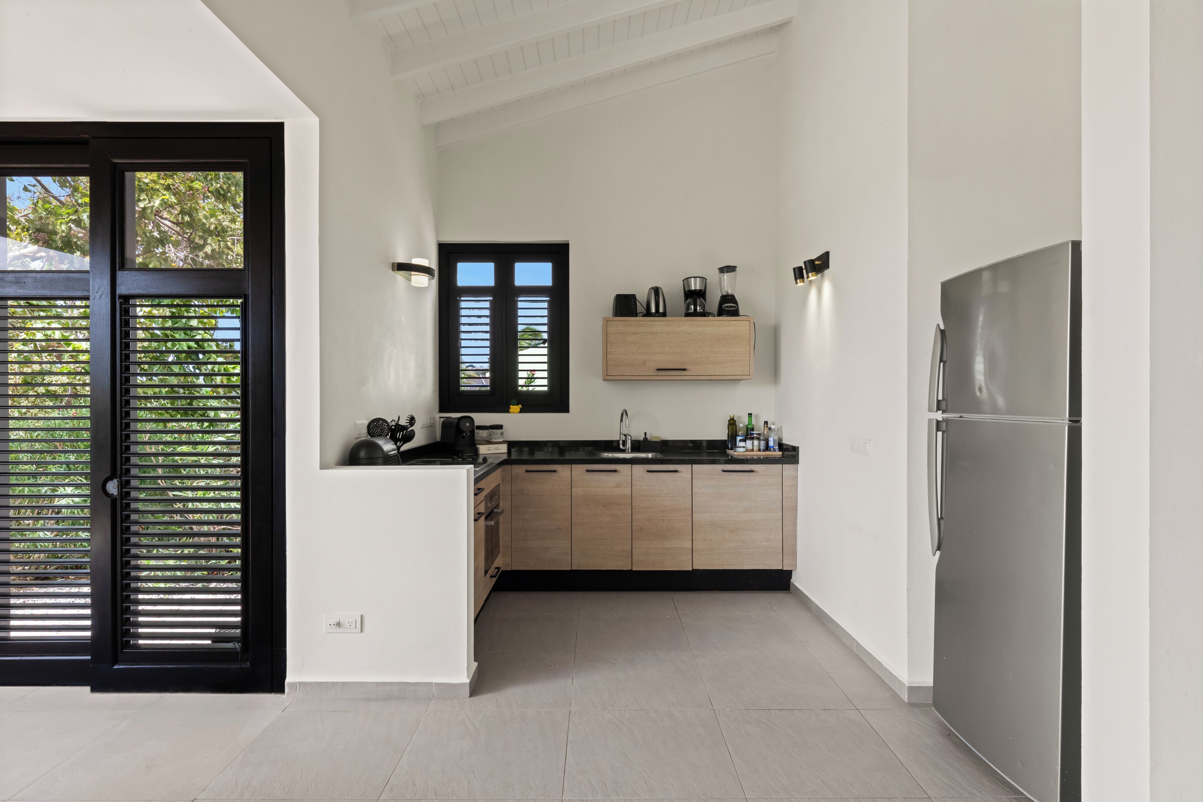 A modern kitchen with a black-framed door, a built-in oven, and a stainless steel refrigerator.