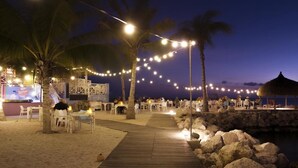 Un área de comedor al aire libre con luces colgantes, palmeras y un paseo de madera.